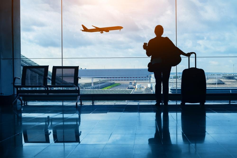 The sillhouette of a woman standing in front of a window in an airport, watching an airplane take off.