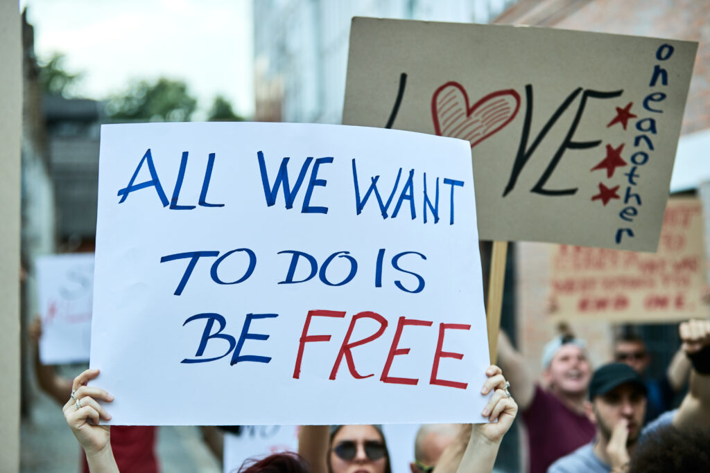 Close-up of a person holding banner with All we want to do is be free inscription while taking a part in a protest for human rights.