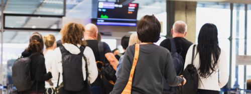 Airport passengers, with their backs to us, looking at their flight status on a screen in the airport