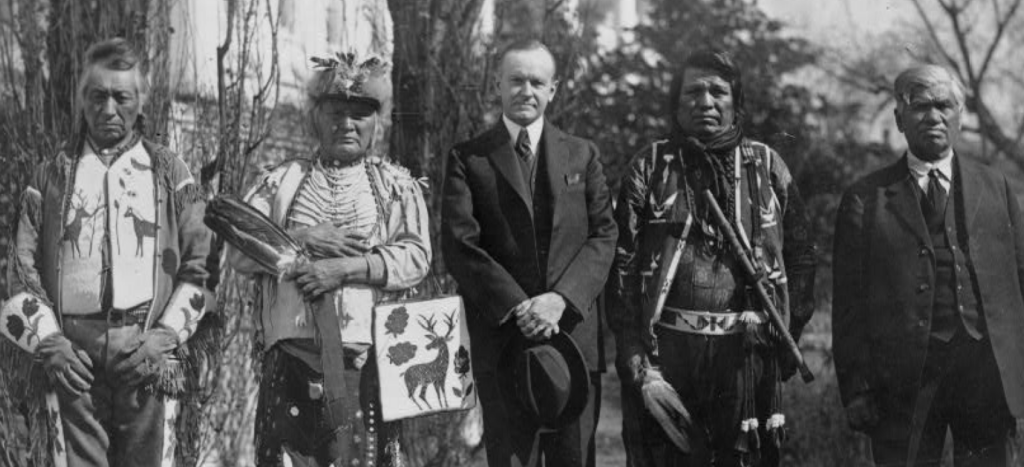 Historical black-and-white photograph accompanying the section on the Indian Citizenship Act of 1924, showing several individuals standing outdoors with President Calvin Coolidge.